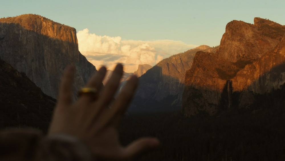 Hand with ring reaching towards sunlit mountains