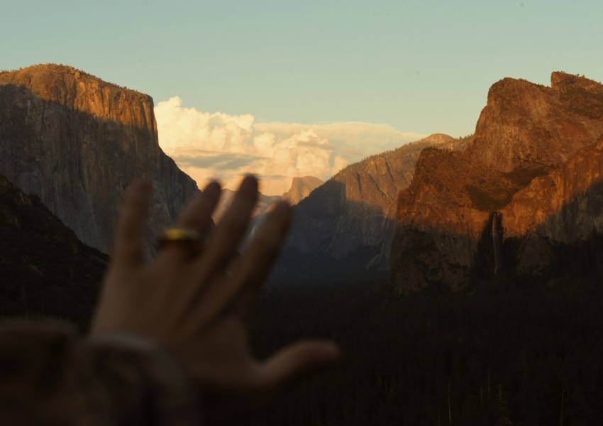 Hand with ring reaching towards sunlit mountains