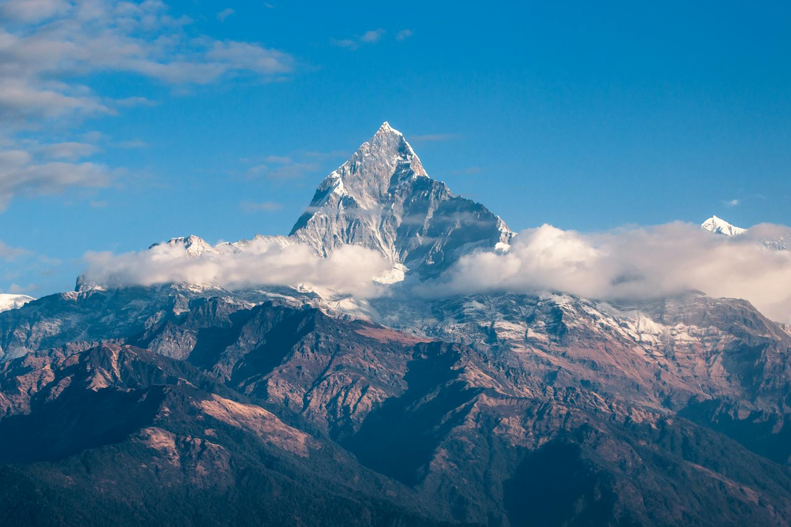 Breathtaking view of a snow-covered mountain peak surrounded by clouds during sunrise.